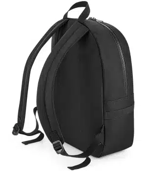 The BagBase Modulr 20L Backpack BG240 is a plain black rucksack featuring a zipped main compartment, two adjustable shoulder straps, a top handle, and a minimalist design without visible logos or extra pockets, shown standing upright on a white background. | Work & Wear DIrect