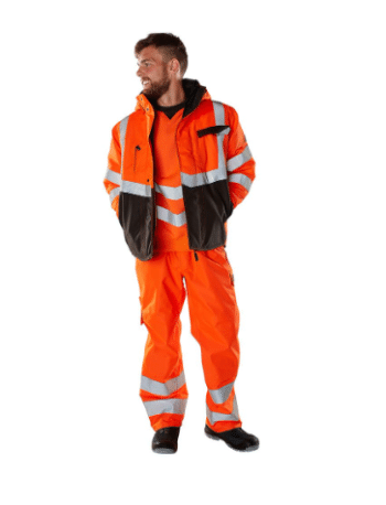  Hastings Winter Jacket—an orange and black high-visibility safety jacket with reflective stripes—and matching trousers, standing slightly turned to the left with his hands in his pockets, gazing off to the side. | Work & Wear DIrect