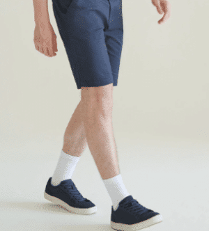 A person wearing navy shorts, white crew socks, and navy trainers is walking against a plain, light-coloured background. Only the lower half of the body is visible. | Work & Wear DIrect